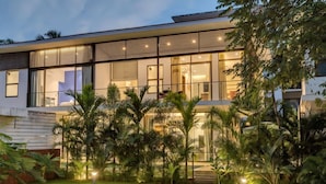 Een modern huis met grote ramen, een verzorgd gazon en tropische planten.
