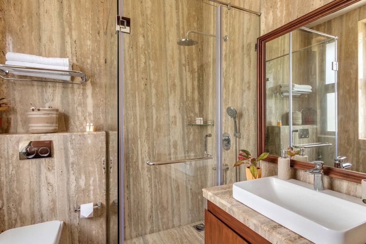 Ein Badezimmer mit einer Glaskabine zur Dusche, einem großen Spiegel und einem weißen Waschbecken.