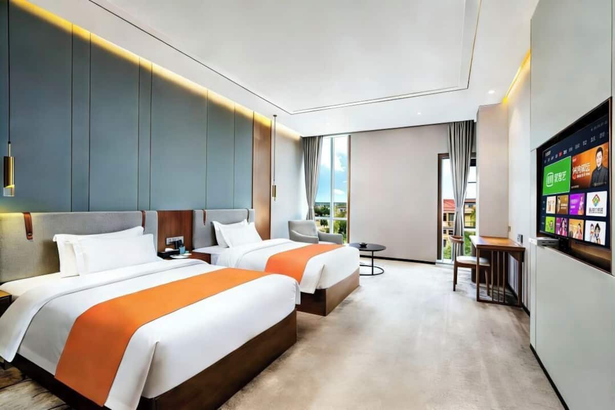 A hotel room with two beds, a TV, a desk, and a view of the outdoors.