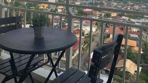 A balcony with a round table and chairs, overlooking a residential area with houses and a distant mountain range. - 1517 Belvedere Samal View and City View (Davao City)