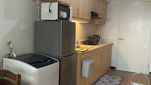 A compact kitchen with wooden cabinets, a stainless steel refrigerator, a microwave, and a small sink. - 1517 Belvedere Samal View and City View (Davao City)