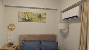 A bedroom with a bed, a nightstand, a wall-mounted air conditioner, a ceiling light, and a painting. - 1517 Belvedere Samal View and City View (Davao City)