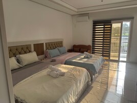 Habitación de hotel con dos camas, un sofá, un ventanal con persianas y vistas al exterior.