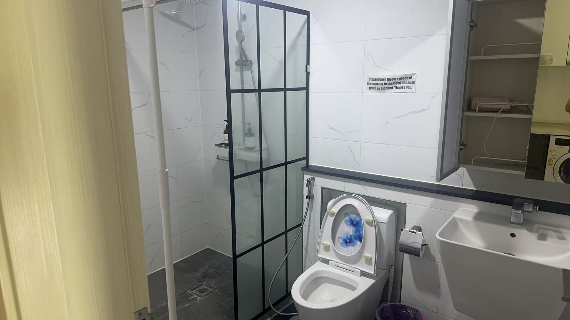 A modern bathroom with a glass-enclosed shower, a toilet with a blue lid, and a sink.