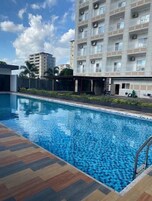 Una piscina con suelo de baldosas en patrón de espiga, rodeada por un edificio con varios balcones y unidades de aire acondicionado.