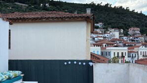 Ein Holztisch mit Stühlen auf einer Dachterrasse, mit Blick auf eine an einen Hügel schmiegt sich liegende Stadt mit Ziegeldächern.
