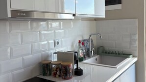 Eine moderne Küche mit weißen Schränken, einer schwarzen Induktionskochplatte, einem eingebauten Backofen und einer Edelstahlspüle.