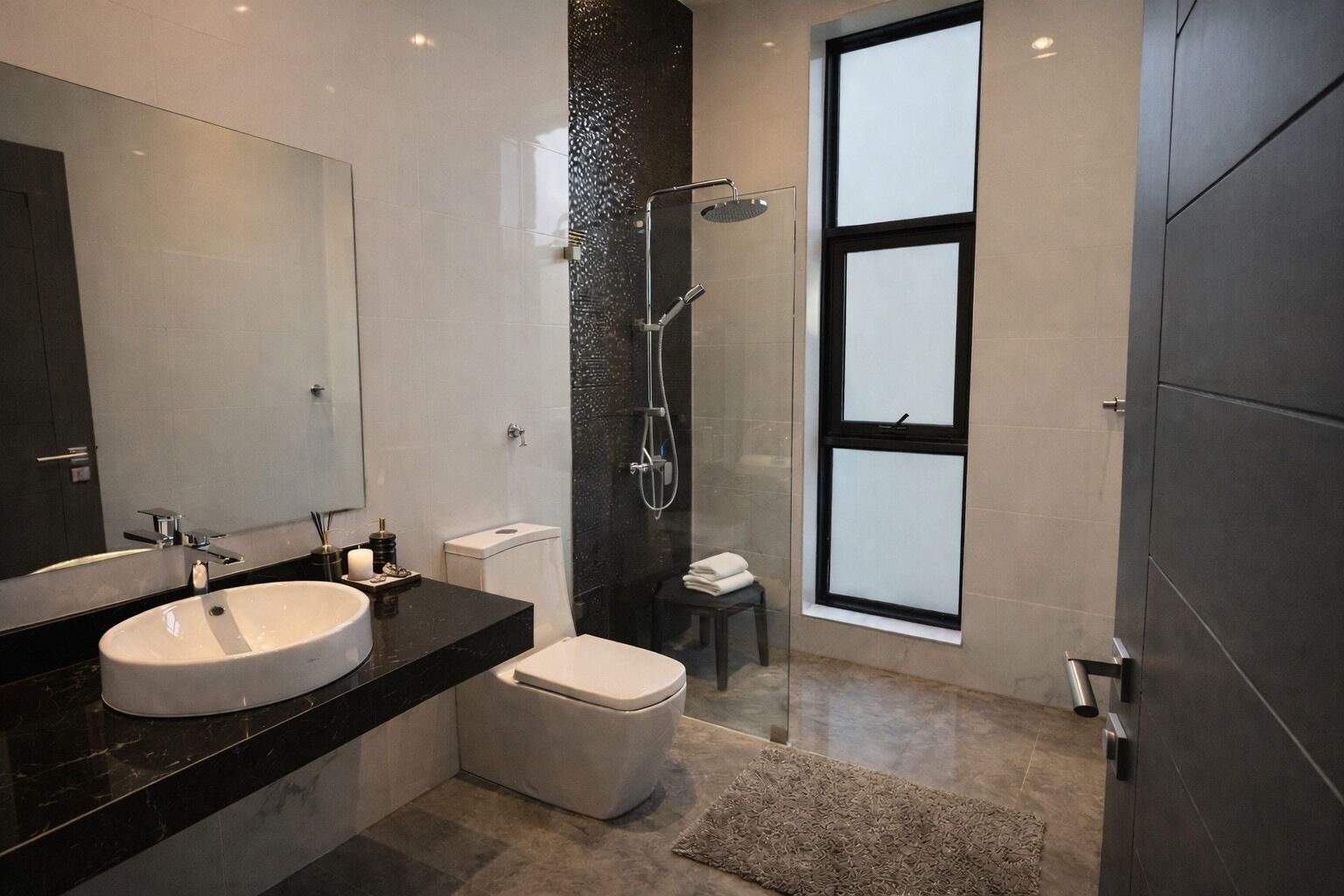Un baño moderno con un espejo grande, un lavabo redondo, inodoro y cabina de ducha con mampara de vidrio.
