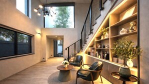 Een moderne woonkamer met een hoge plafond, een trap en een boekenplank vol boeken en decoratieve objecten.