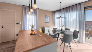 A modern kitchen with a wooden countertop, a dining area with a round table and chairs, and a large window with curtains. - Apartment Near Beach With sea View (Porec)