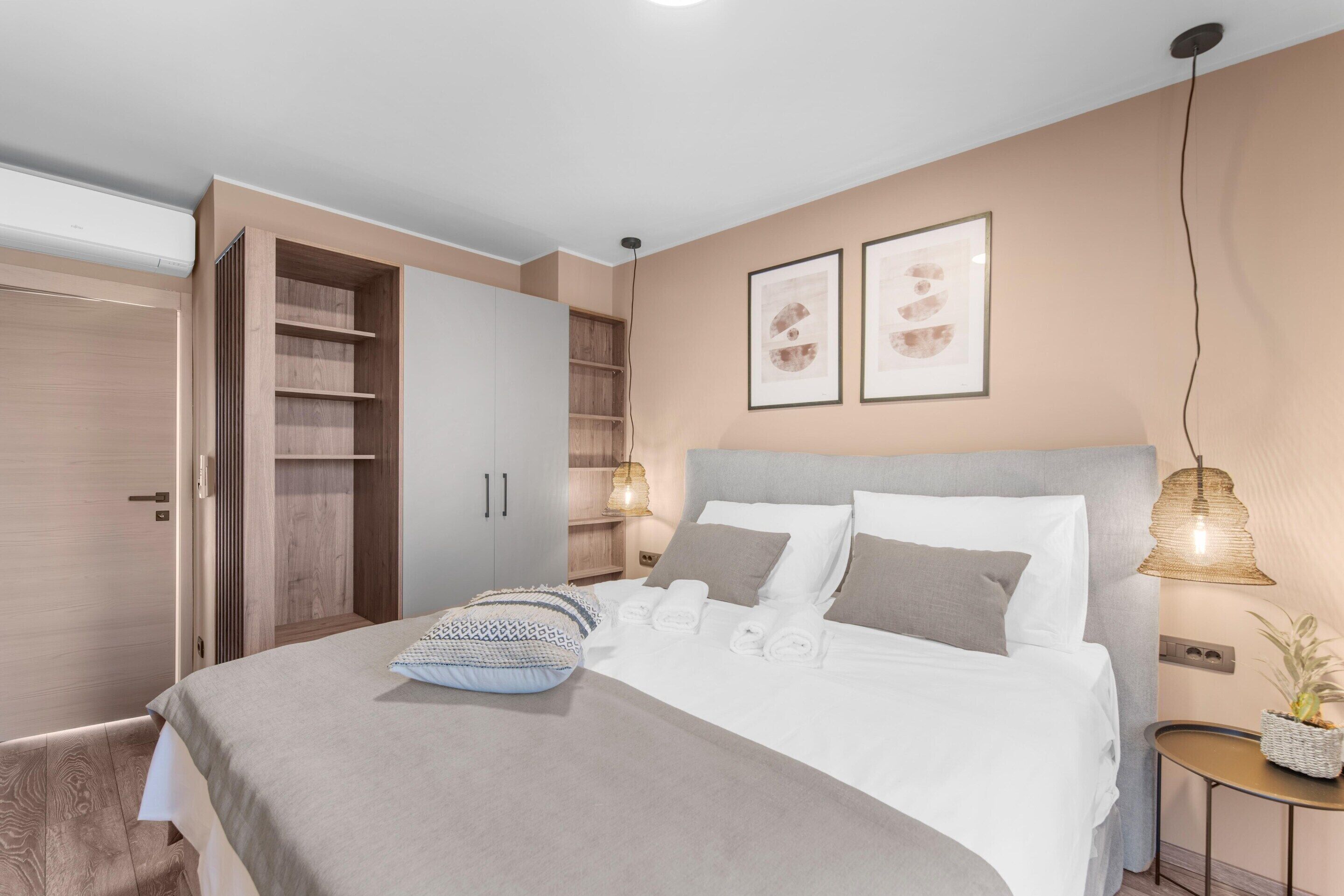 A modern bedroom with a large bed, a wardrobe, and a bedside table with a lamp.