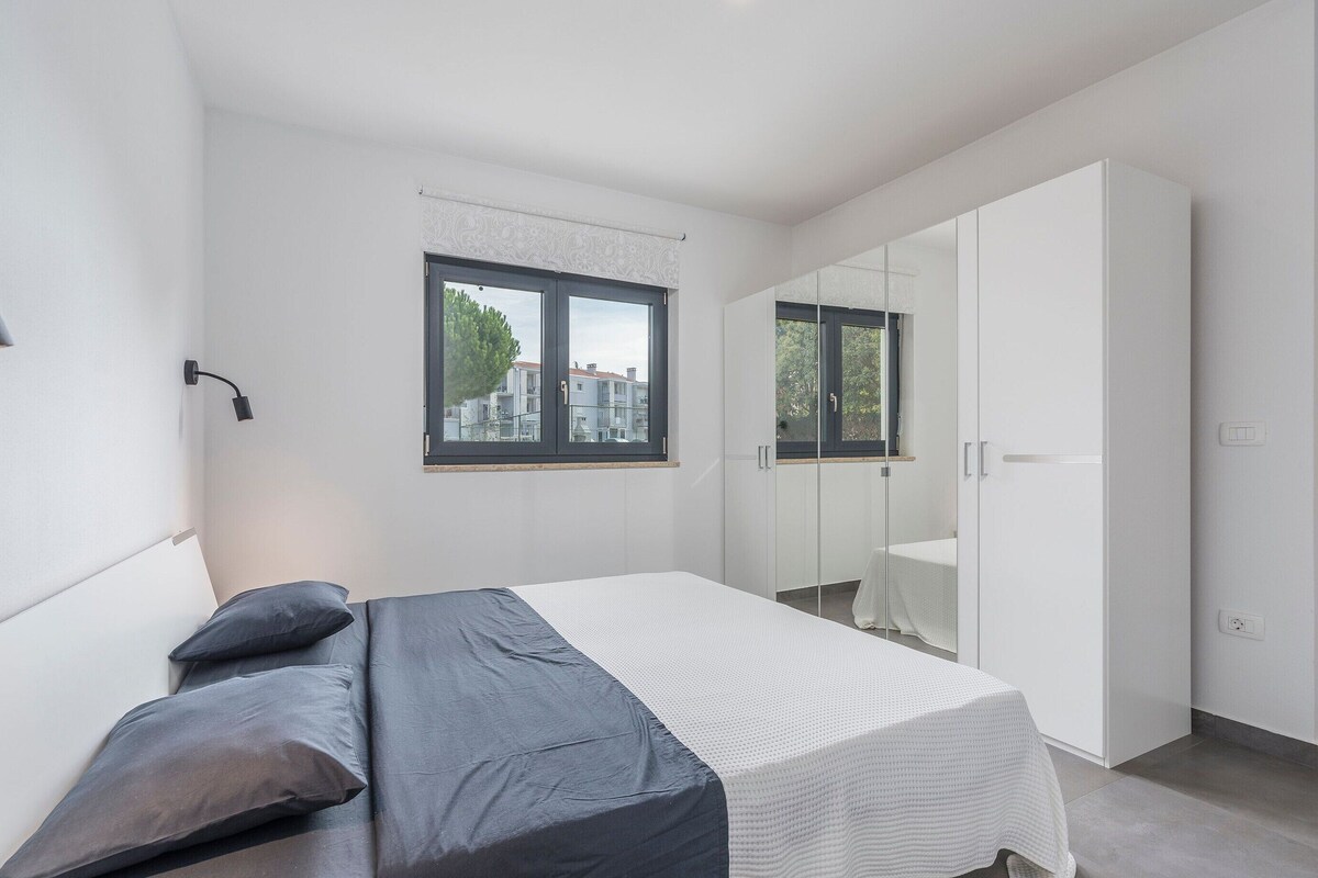 A modern bedroom with a bed, a wardrobe, a window, and a mirror.
