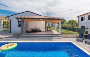 Ein modernes Haus mit überdachter Terrasse, einem Swimmingpool und Gartenmöbeln.