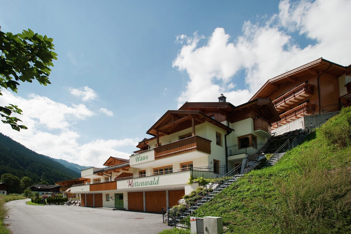 A multi-story hotel with balconies, a visible name 'Haus Mittenwald,' and a parking area.