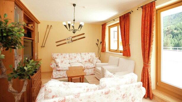 A cozy living room with floral-patterned sofas, a wooden cabinet, and a ski rack on the wall. - Chalet in Saalbach Near Ski Lift (Saalbach-Hinterglemm)