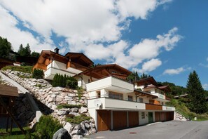A multi-story chalet with a stone retaining wall, wooden balconies, and a garage. - Chalet in Saalbach Near Ski Lift (Saalbach-Hinterglemm)