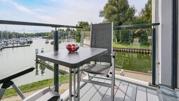 Ein Balkon mit Tisch und Stühlen, mit Blick auf einen Jachthafen mit Booten und einem Fluss.