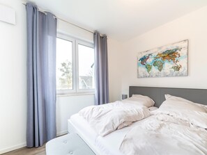 A bedroom with a bed, grey curtains, a world map artwork, and a window with a view of a house. - Liebevoll Eingerichtetes Appartement (Rechlin)