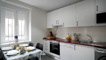 Cocina compacta con armarios blancos, encimera roja y comedor con mesa lista para dos.