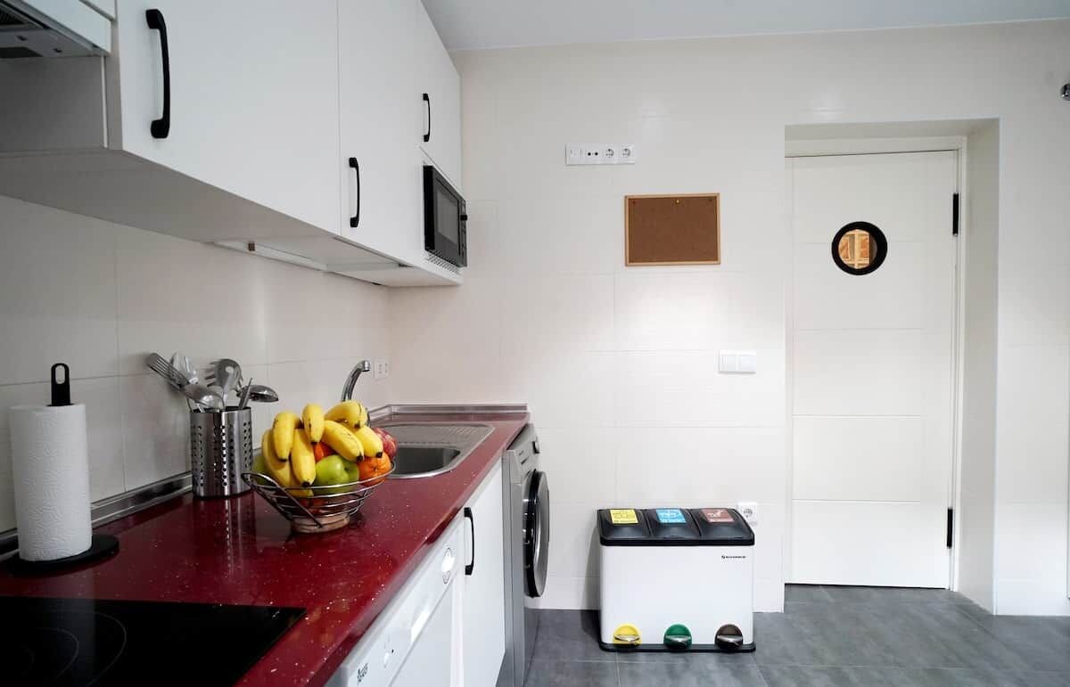A kitchen with white cabinets, a microwave, a sink, and a small trash bin.