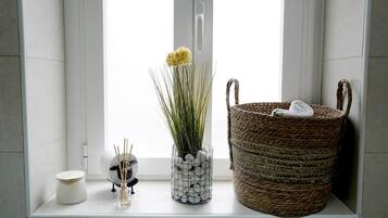Un lavabo da bagno con una vasca bianca in ceramica, un cesto intrecciato e una pianta decorativa in un cestino metallico.