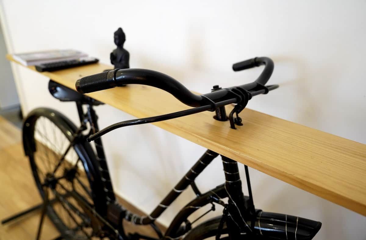 Un vélo avec une selle en bois fixée à un mur, un guidon noir et un cadre noir.