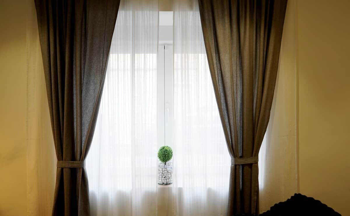 A room with a window covered by curtains, a small potted plant on the windowsill, and a wooden floor.