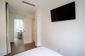 A bedroom with a bed, a TV mounted on the wall, and a door leading to a bathroom. - Murallas Home (Ávila)