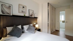 Un lit bien fait, avec des oreillers, une lampe de chevet et des œuvres d’art encadrées accrochées au mur.