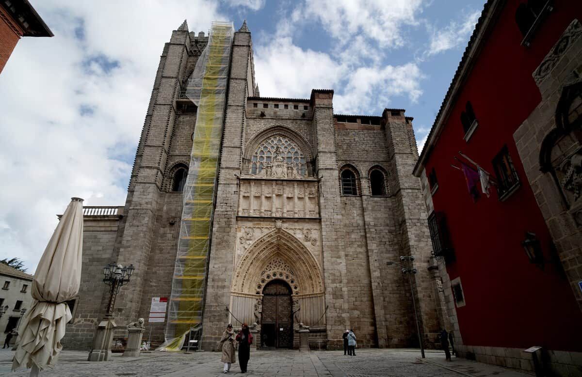 Un edificio histórico con una entrada destacada, una torre alta y un edificio rojo a la derecha.
