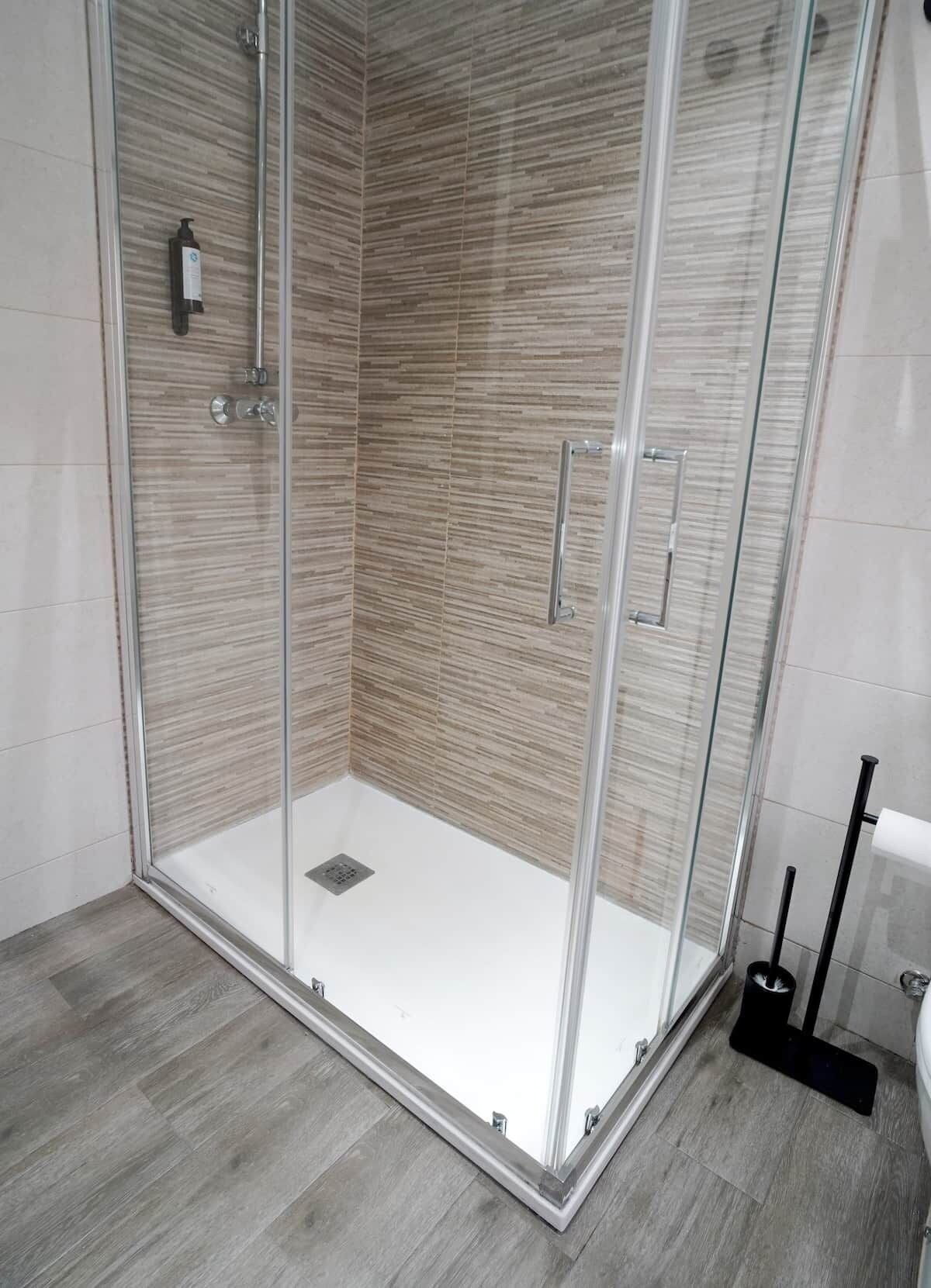 Une douche fermée par des parois en verre, avec un sol carrelé et une douchette à main.