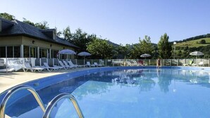 A swimming pool with lounge chairs and umbrellas, surrounded by a building with a tiled roof. - Apartment in Saint-geniez by Lot River (Saint-Geniez-d'Olt-et-d'Aubrac)