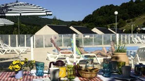 A poolside area with lounge chairs, a table with drinks and snacks, and a view of a pool and hills in the background. - Apartment in Saint-geniez by Lot River (Saint-Geniez-d'Olt-et-d'Aubrac)