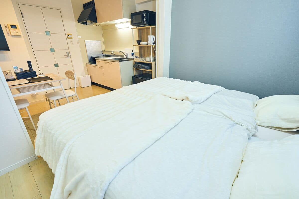 Una habitación de hotel pequeña con cama, escritorio con silla, kitchenette y baño.