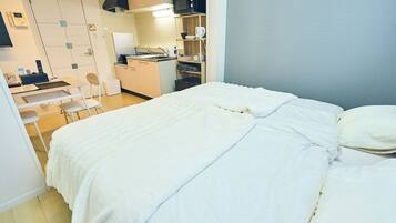 A compact hotel room with a bed, a desk with a chair, a kitchenette, and a bathroom.