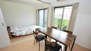 A compact room with a bed, a dining table, four chairs, and large windows. - Sakurakan (Kagoshima)
