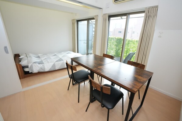 A compact room with a bed, a dining table, four chairs, and large windows. - Sakurakan (Kagoshima)