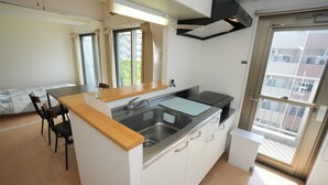A compact kitchen with a sink, a small countertop, and a window with curtains. - Sakurakan (Kagoshima)