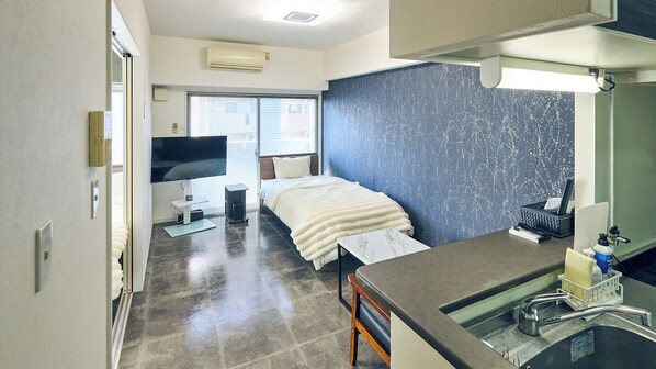 Quarto de hotel com uma cama, uma secretária com pia, televisão e janela com persianas.
