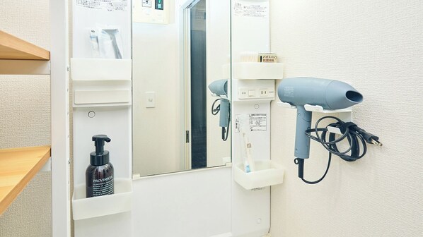 A bathroom with a hairdryer mounted on the wall, a mirror, and a bottle of Provinscia shampoo. - Sakurakan (Kagoshima)