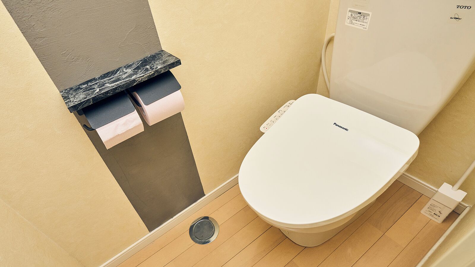 A toilet with a white seat and lid, a black marble countertop, and a roll of toilet paper dispenser.