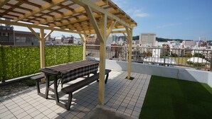 A rooftop terrace with a pergola, a checkered table, and a bench. - Sakurakan (Kagoshima)