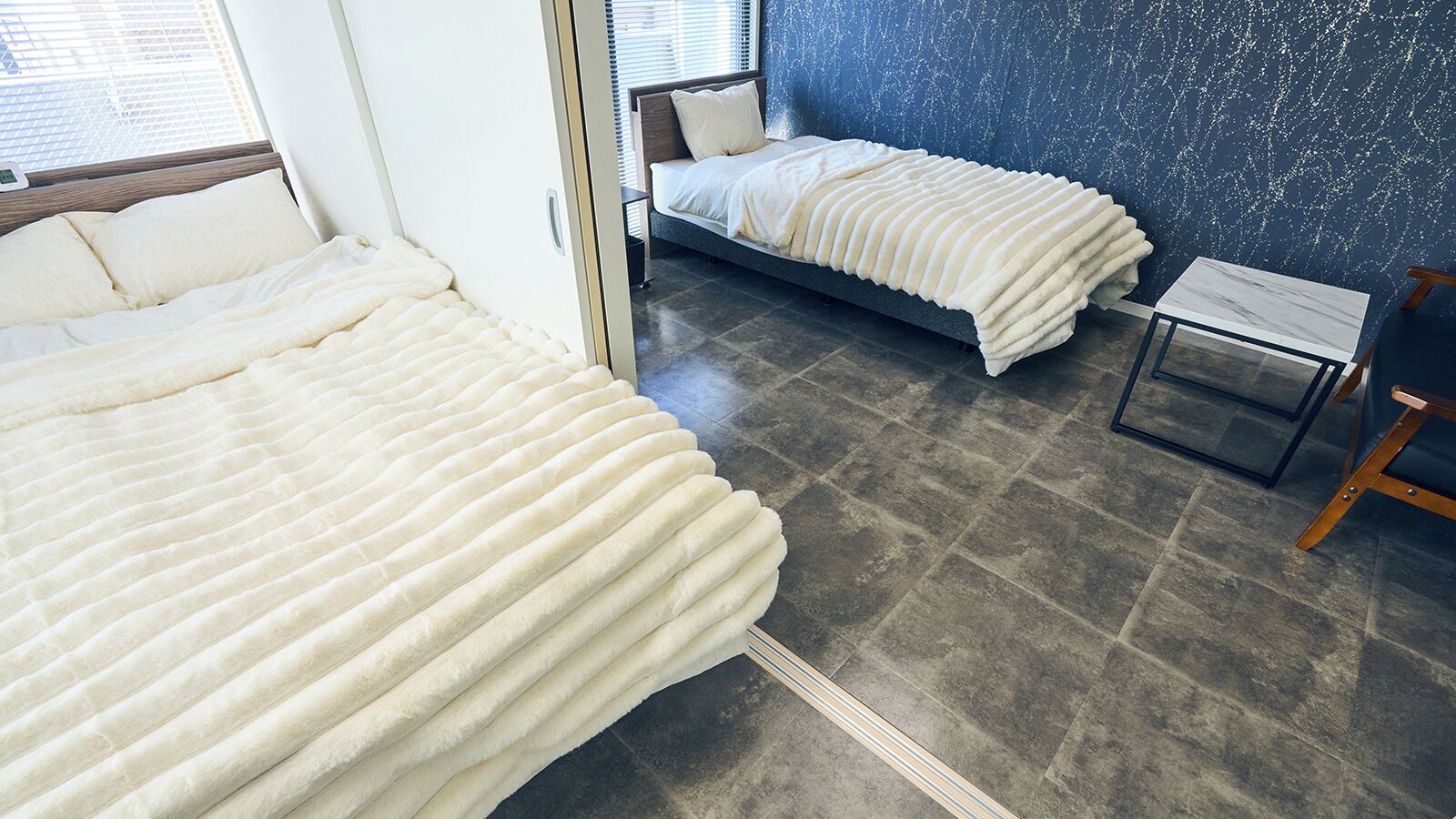 A bedroom with two beds, a small table, and a chair.