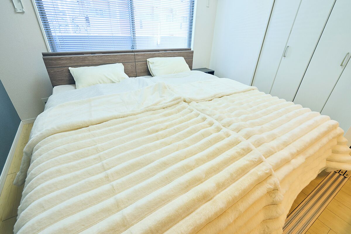 A neatly made bed with a white duvet and pillows, a wooden headboard, and a window with blinds.
