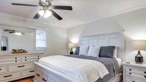 Ein Schlafzimmer mit Bett, Nachttischen, einem Schminktisch, einem Deckenventilator und einem Fenster mit Jalousien.