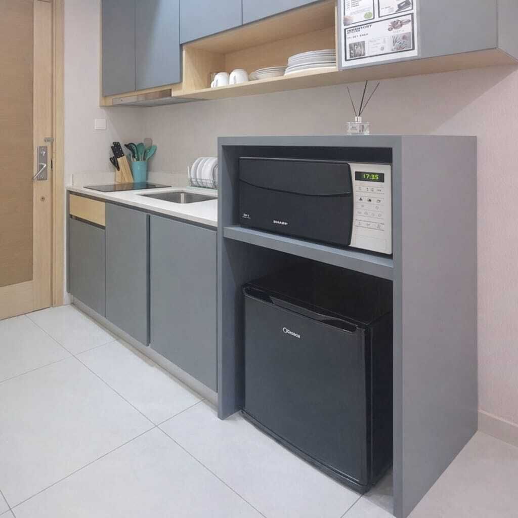 Una cocina compacta con armarios grises, un microondas integrado y un refrigerador pequeño.