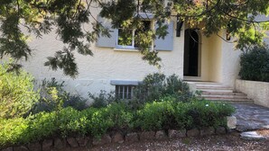 Una casa con una scala in pietra che conduce a un ingresso scuro, circondata da vegetazione lussureggiante e un muro di pietra.
