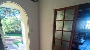 Un corridoio con pavimento piastrellato che conduce a una stanza con una porta in legno e una finestra.