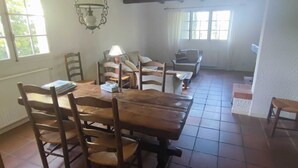 Zona pranzo con tavolo e sedie in legno, lampadario e ampie finestre che lasciano entrare luce naturale.