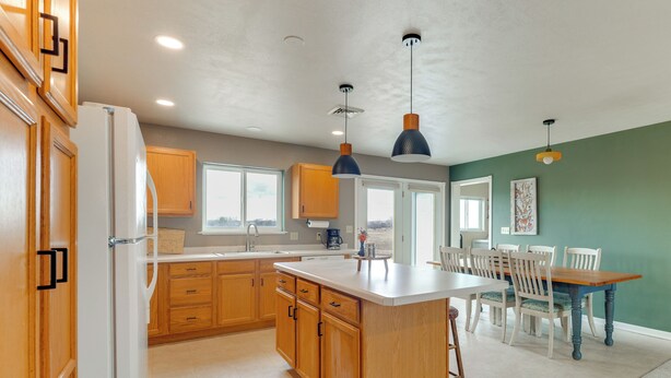 Une cuisine moderne avec des meubles en bois, un réfrigérateur blanc et des luminaires suspendus.